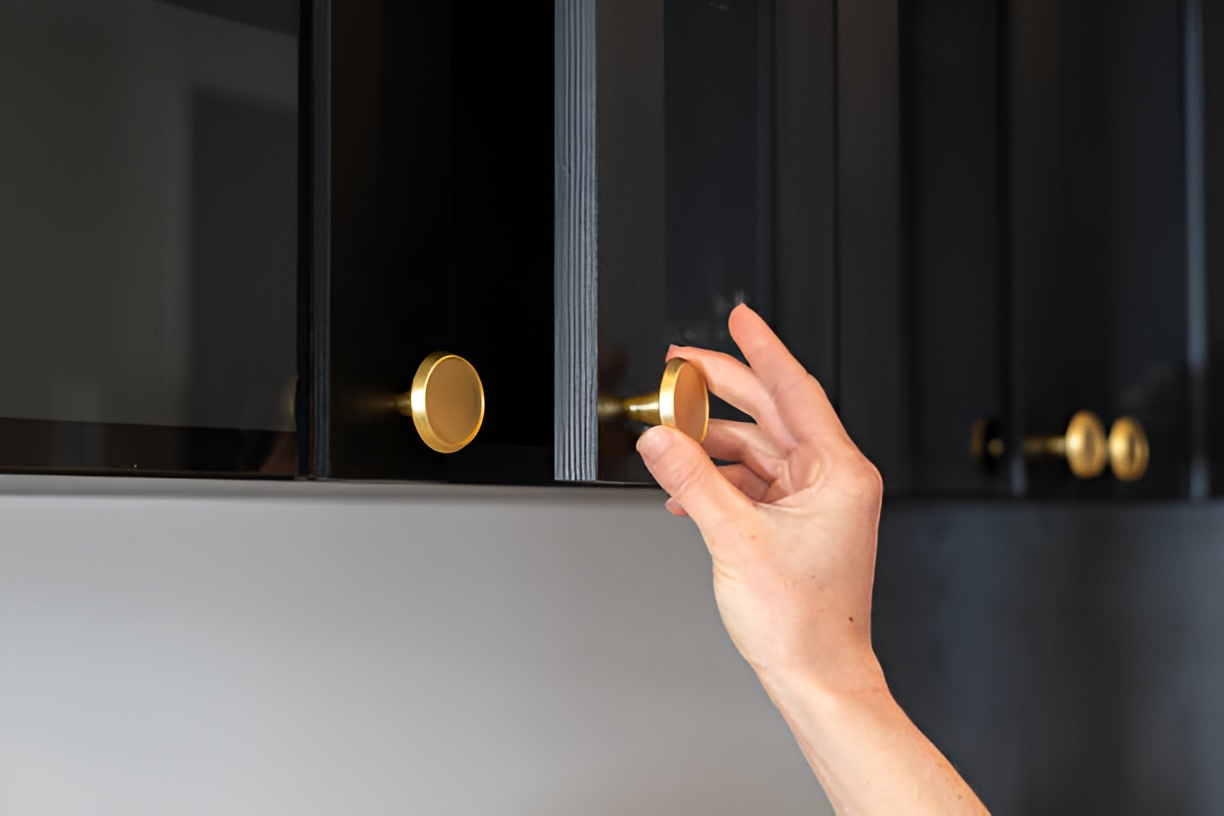 woman opening a black kitchen cabinet door with a gold handle